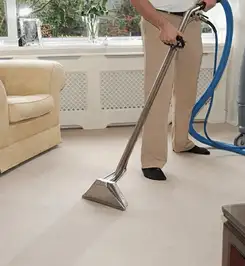 Professional carpet cleaner using a hot-water extraction wand and hose machine in a living room in Nashua, NH.
