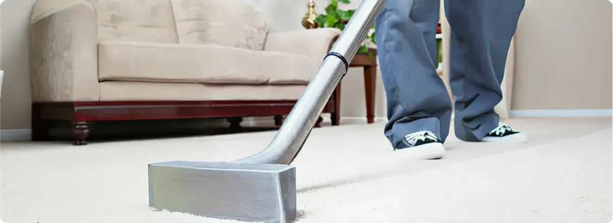 Carpet cleaning technician using a hot-water extraction wand on a light-colored carpet in a living room, Nashua, NH.