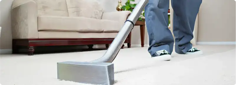Carpet cleaning technician using a hot-water extraction wand on a light-colored carpet in a living room, Nashua, NH.