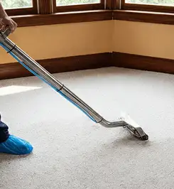 Steam carpet cleaning technician using a hot-water extraction wand on a residential carpet, wearing blue protective shoe covers Nashua, NH.
