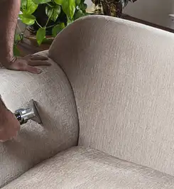 Professional upholstery cleaner deep-cleaning a fabric sofa with a handheld extraction tool and hose Nashua, NH.